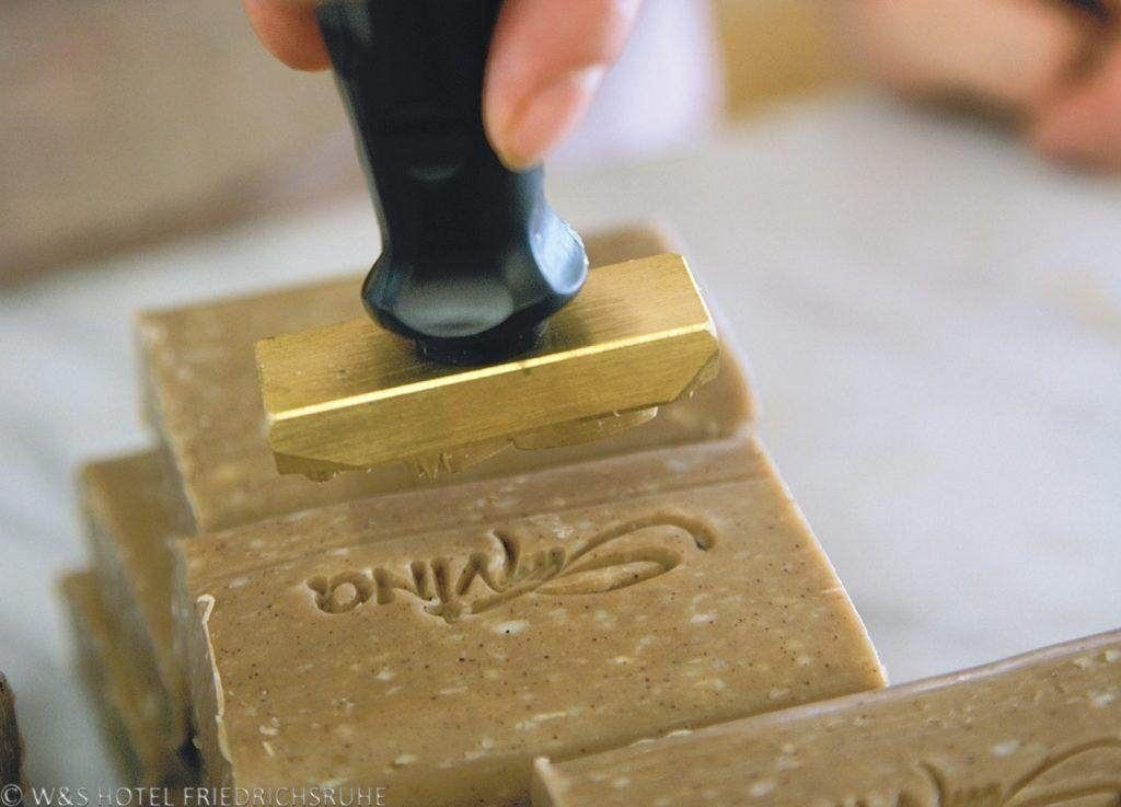 Ein Stempel mit dem Namen einer Naturkosmetikmarke "San Vino" wird auf ein Stück Oliven-Seife gepresst.