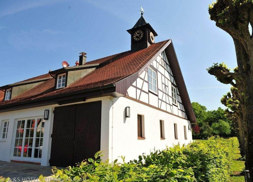 Ein Seitenblick auf ein weißes Fachwerkhaus mit kleinem Glockenturm und großer Glasfront.