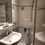 Ein kleines Badezimmer in Den Haag mit weißen Fliesenwänden und blauen Akzenten. Es verfügt über ein Waschbecken mit Spiegel, ordentlich gefaltete Handtücher, eine Toilette und Toilettenartikel auf der Ablagefläche.