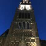 Beleuchteter Kirchturm im gotischen Stil vor einem dunkelblauen Abendhimmel in Den Haag, mit Bogenfenstern und detailliertem Mauerwerk.