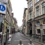 Eine schmale Straße in Den Haag, gesäumt von historischen Gebäuden und an den Seiten geparkten Fahrrädern. Schilder weisen auf eine Fußgängerzone und Hotelanweisungen hin.