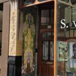 Der Eingang eines Gebäudes in Den Haag zeigt dekorative Kacheln mit floralen Mustern. Daneben befindet sich ein großes Schaufenster, das mit ausgestellten Büchern auf einen Buchhändler hindeutet.