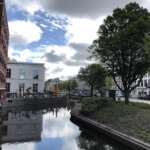 Ein Kanal in Den Haag ist unter einem teilweise bewölkten Himmel von Bäumen und Gebäuden gesäumt.