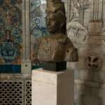 Eine bronzene Frauenbüste auf einem Sockel ziert den Friedenspalast in Den Haag, vor einer wunderschön dekorierten Fliesenwand.