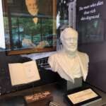 Ausstellung mit einem Porträt, einer Büste, einem Buch und einem Hammer in Den Haag. Der Text lautet: „Wer so reich stirbt, stirbt in Schande.“