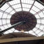 Blick auf eine große, kreisförmige Glasdecke mit einer zentralen Metallstruktur und Holzpaneelen, die an die architektonische Eleganz Den Haags erinnert.