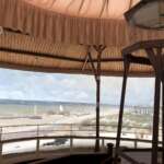 Innenansicht eines runden Gebäudes mit einem Panorama der historischen Küstenlandschaft Den Haags, das einen Strand, Meer, Boote und entfernte Gebäude unter einem bewölkten Himmel zeigt.