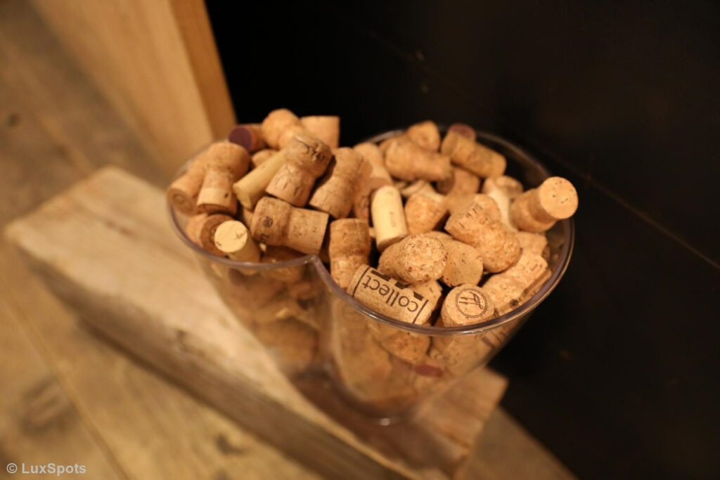 Ein durchsichtiger Glasbehälter, gefüllt mit zahlreichen Weinkorken, auf einer Holzoberfläche platziert.