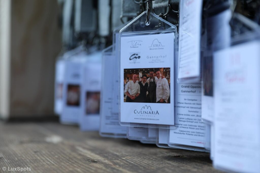 Nahaufnahme von Einlassschildern, die an Haken hängen. In der Mitte sind Veranstaltungsdetails und ein Foto von den Organisatoren des Events zu sehen.