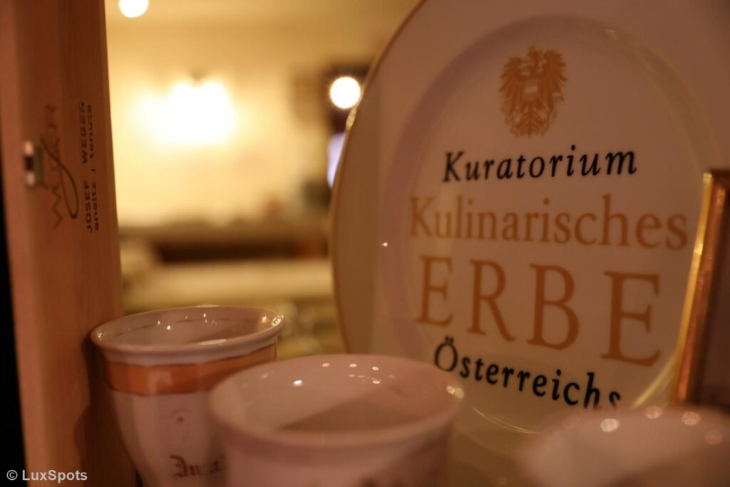 Nahaufnahme eines Tellers mit der Aufschrift „Kulinarisches Erbe Österreichs“ und dekorativen Tassen in sanfter Beleuchtung.