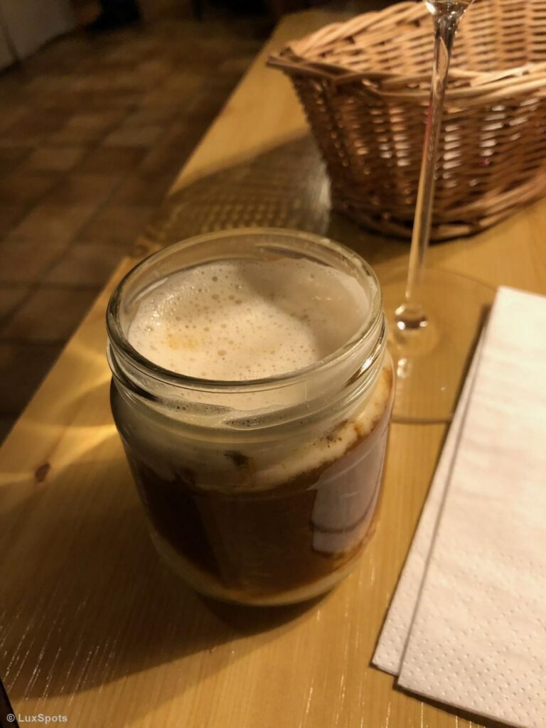 Ein Einmachglas mit schaumiger Flüssigkeit gefüllt auf einem Holztisch, neben einer gefalteten Serviette und einem Korb.