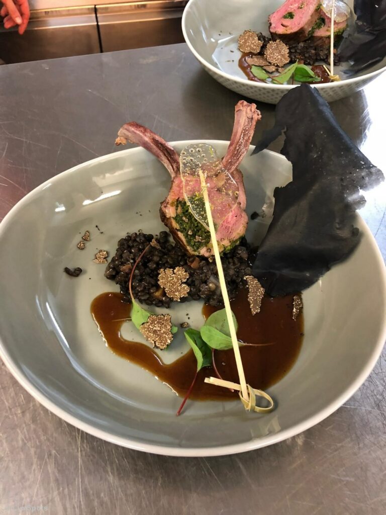 Lammkarree auf Linsen, garniert mit Microgreens, schwarzen Trüffelscheiben und einer dunklen Sauce.