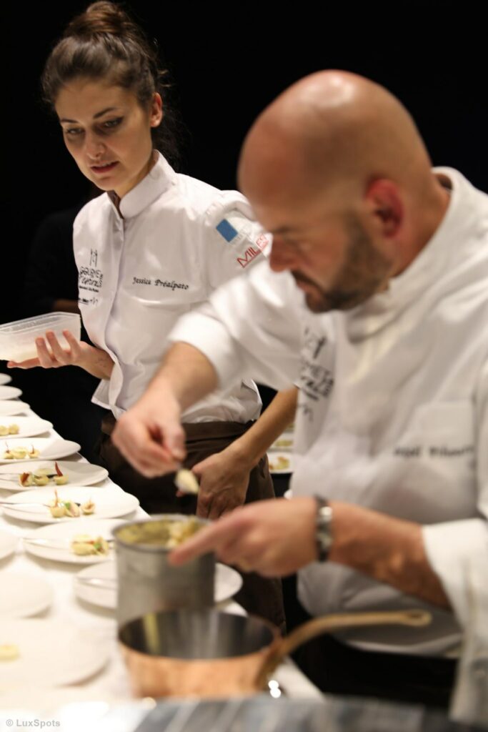 Zwei Köche in weißen Uniformen konzentrieren sich in einer Küche auf das Anrichten von Gerichten.
