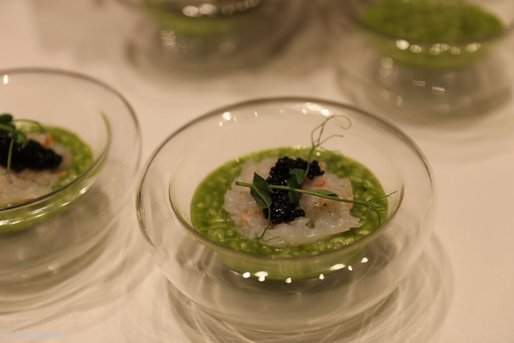 Ein Gericht aus grünem Risotto, garniert mit Garnelen und schwarzem Kaviar in einer Glasschüssel.