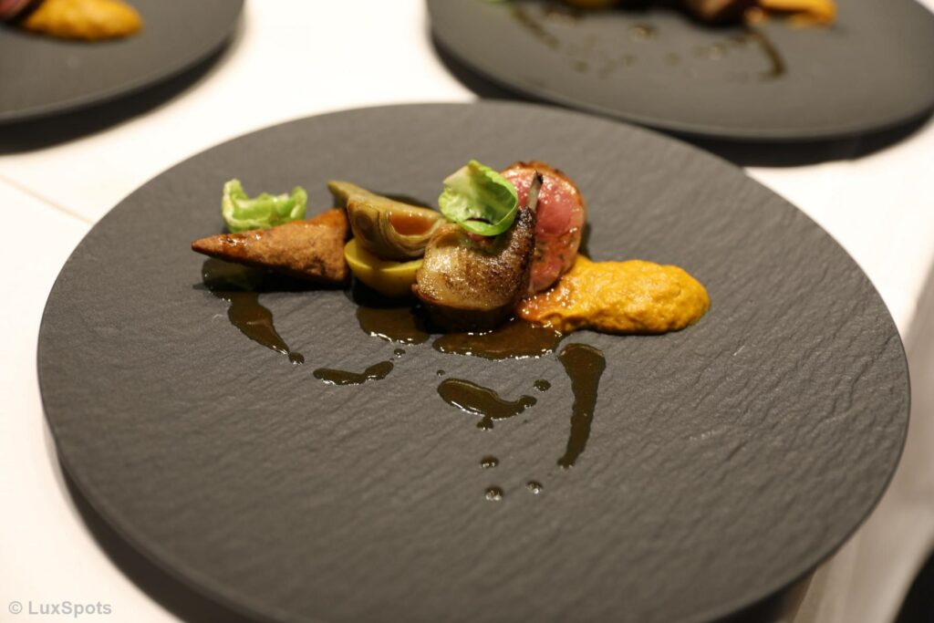 Gourmetgericht mit Taube, Soße und Gemüsepüree garniert auf einer Schieferplatte.