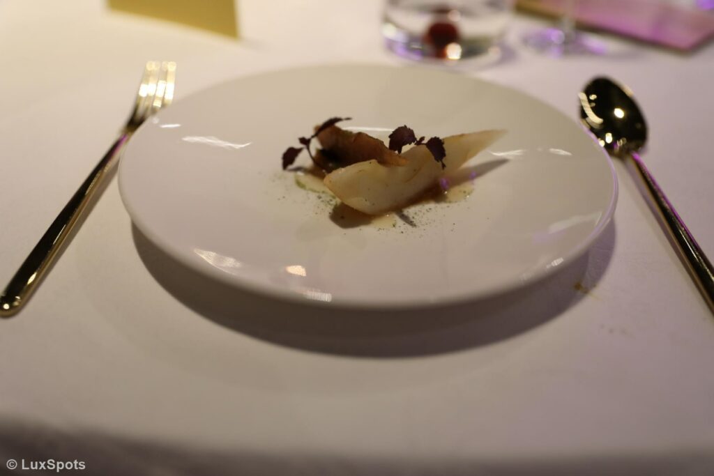 Ein feines Dessert mit kunstvoll angerichteten Birnen auf einem weißen Teller, gedeckt auf einer weißen Tischdecke, mit Gabel und Löffel auf beiden Seiten.