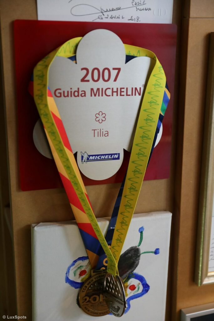 An einer Wand hängende Plakette des Guide Michelin für das Jahr 2007 mit zwei weiteren davor hängenden Medaillen.