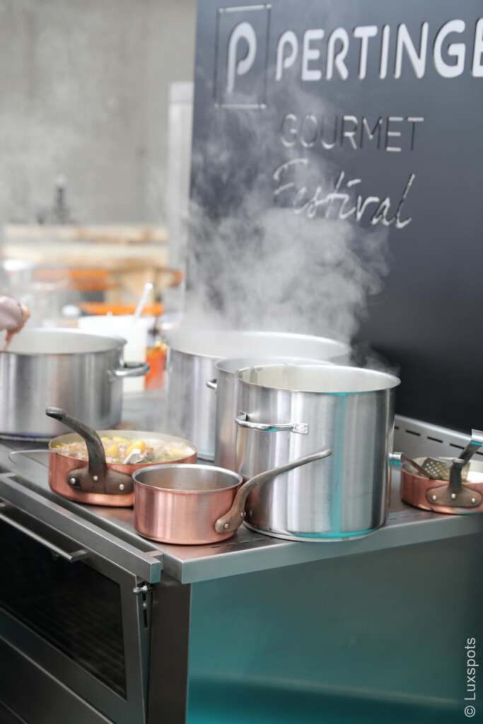 Eine Kücheneinrichtung mit dampfenden Töpfen und Kupferpfannen auf einem Herd bei einem Gourmetfestival.