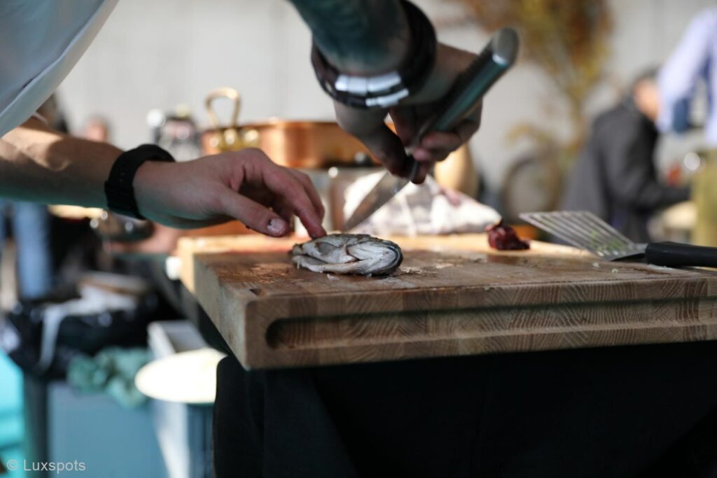 Person schneidet in einer Küche einen Fisch auf einem hölzernen Schneidebrett.