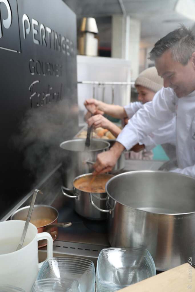 Köche rühren in einer Außenküche in Töpfen auf dem Herd, Dampf steigt auf.