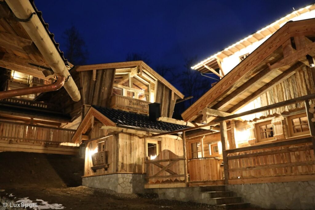 Rustikale Holzhütten mit beleuchteten Balkonen und Dächern heben sich von einem dunklen Abendhimmel ab.