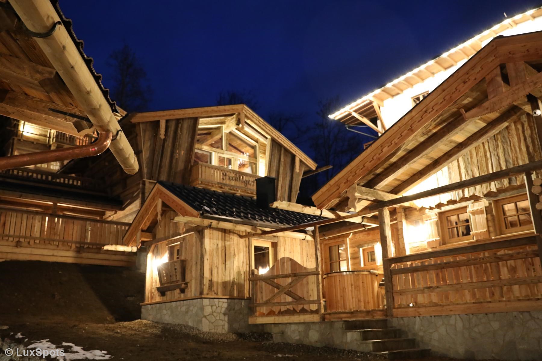 Rustikale Holzhütten mit beleuchteten Balkonen und Dächern heben sich von einem dunklen Abendhimmel ab.