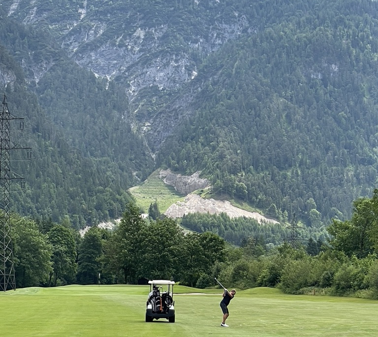 Golfspieler mit Golfcart vor Bergmassiv im Golfclub Gut Brandlhof