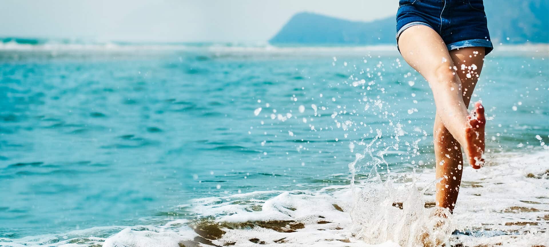Eine Frau läuft am Strand entlang und spritzt mit Wasser.
