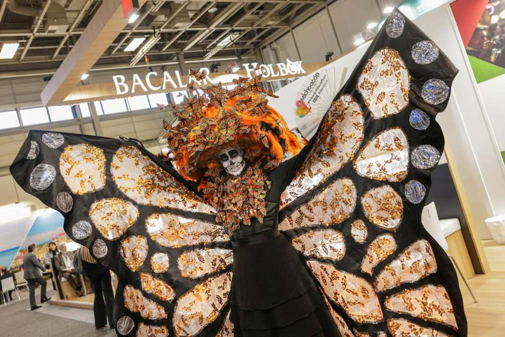 Person, die ein aufwendiges Schmetterlingskostüm mit orangefarbenen und schwarzen Flügeln trägt und in einer Kongresshalle steht.