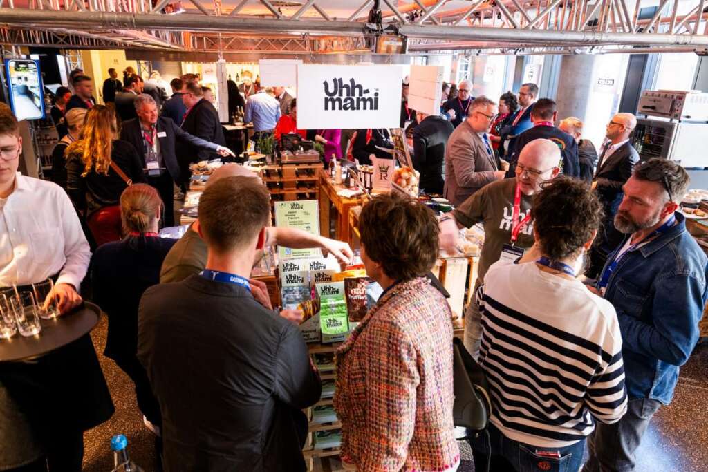 Menschen stehen bei einer gut besuchten der Gastro Vision in Hamburg an einem Stand, an dem Produkte von „Uhh-Mami“ präsentiert werden, und unterhalten sich.