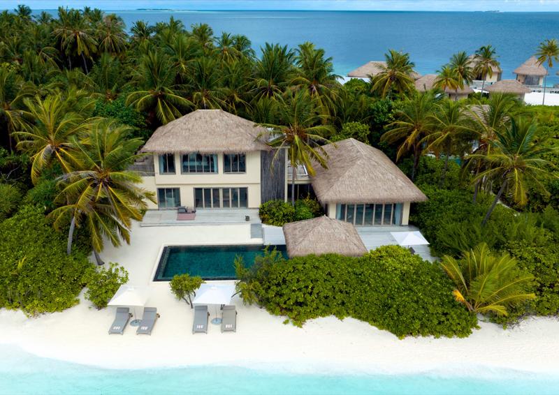 Luftaufnahme einer luxuriösen Strandvilla auf einer tropischen Insel mit Palmen, weißem Sandstrand und einem privaten Pool.