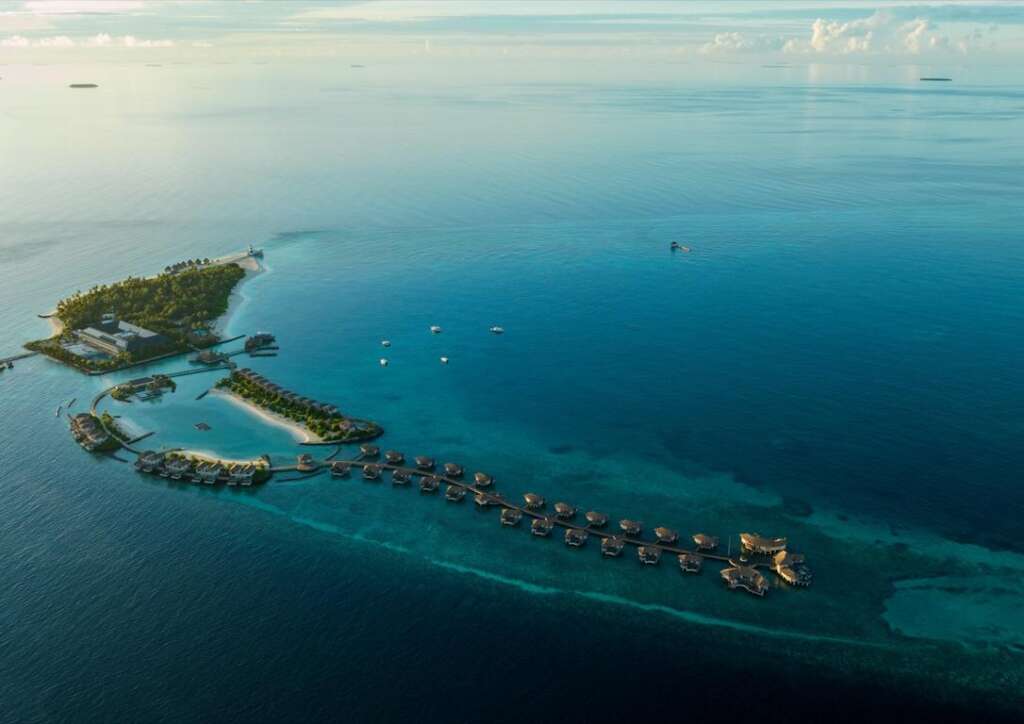 Luftaufnahme eines exklusiven Inselresorts mit Wasserbungalows und üppiger Vegetation, umgeben vom türkisfarbenen Meer.