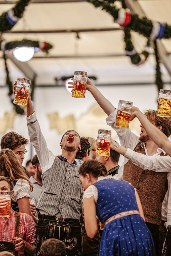 Fröhliche Menschen strecken ihre Bierkrüge in die Luft und singen gemeinsam in einem Festzelt auf dem Oktoberfest.