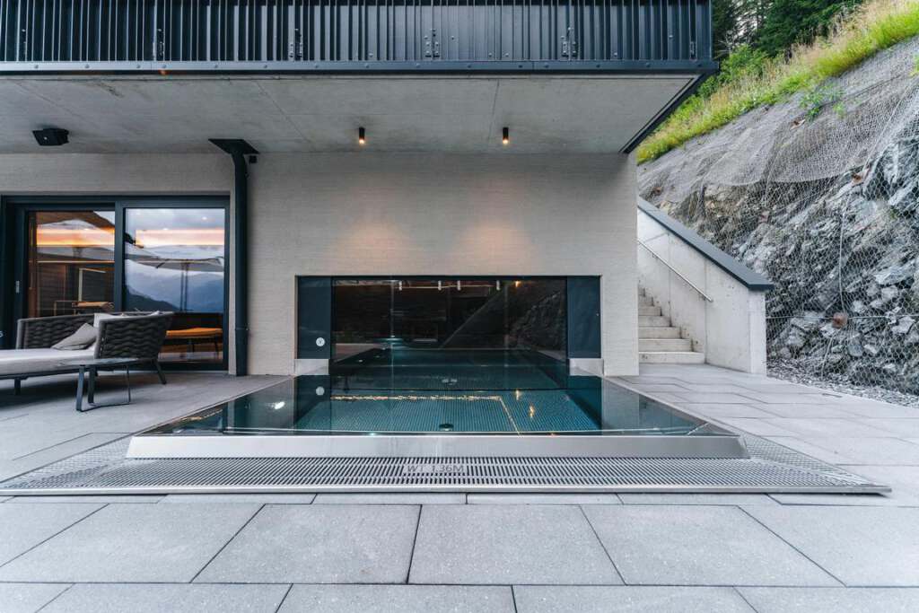 Außenterrasse mit kleinem rechteckigen Pool, angrenzenden Treppen und einer modernen Lounge-Einrichtung neben einer Glastür. Auf der rechten Seite ist ein schroffer Hügel zu sehen.