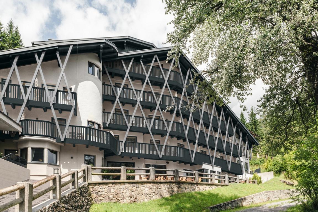 Ein großes, leicht spitz zulaufendes Gebäude in weiß mit dunkelgrünen Verstrebungen und Balkonen.