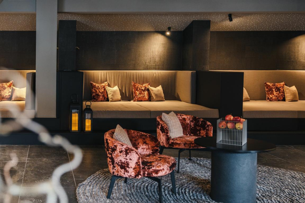 Designter Loungebereich eines Hotels in St. Anton am Arlberg, mit rosaroten Samtsesseln, tiefe, beigefarbene Couches, die angestrahlt werden und dunkler Steinboden.