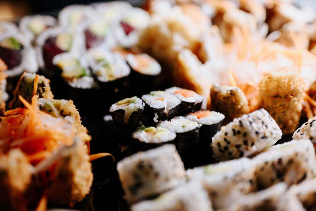 Eine Nahaufnahme verschiedener Sushi-Rollen, darunter mit Nori umwickelte und mit Sesam überzogene Varianten, garniert mit geraspelten Karotten.