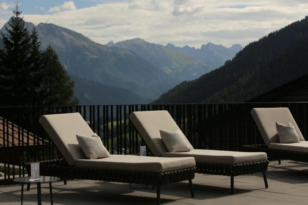 Drei Sonnenliegen stehen auf einer Terrasse. Im Hintergrund ist das sommerliche Alpenpanorama in Österreich zu sehen.