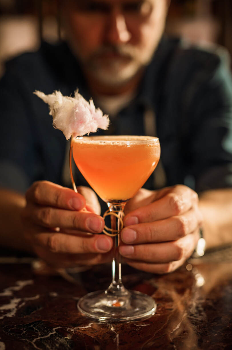 In der Alcron Bar in Prag hält eine Person elegant einen mit rosa Böüten garnierten Cocktail in einem schicken Coupe-Glas.
