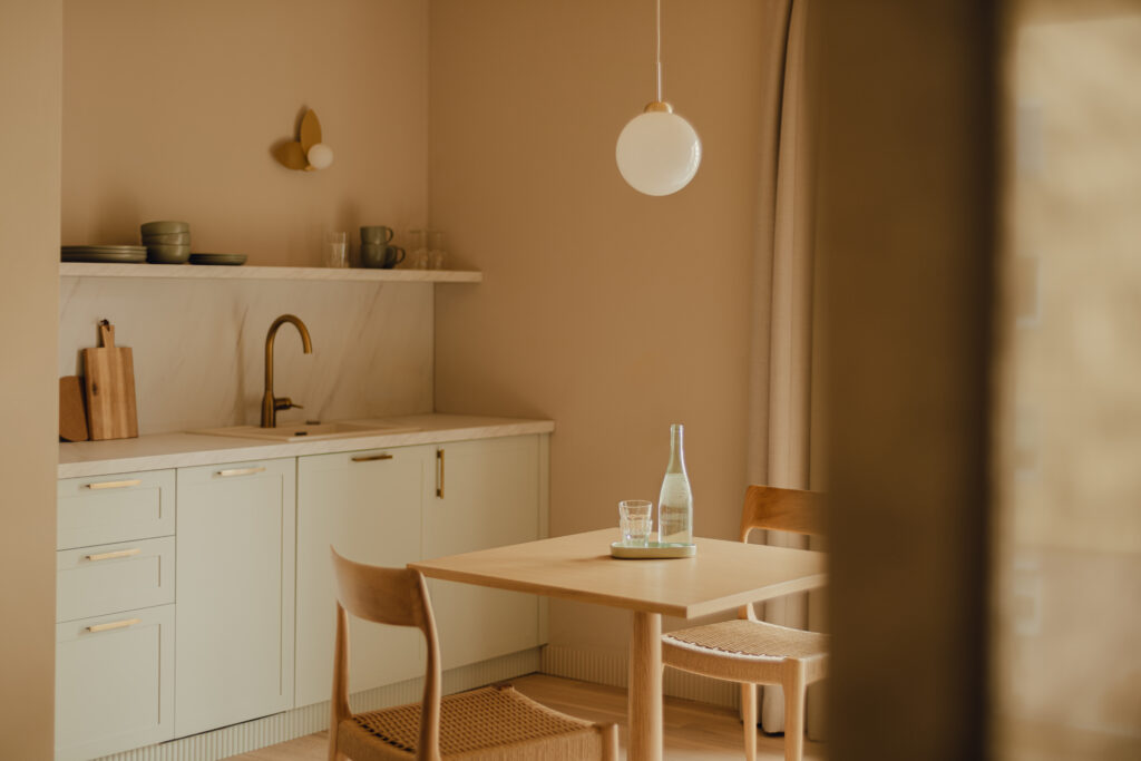 Diese minimalistische Küche verfügt über einen Esstisch aus hellem Holz mit zwei Stühlen. Eine Flasche und ein Glas stehen bereit, während weiße Schränke, eine Marmorrückwand und eine Hängelampe das anspruchsvolle Dekor vervollständigen.