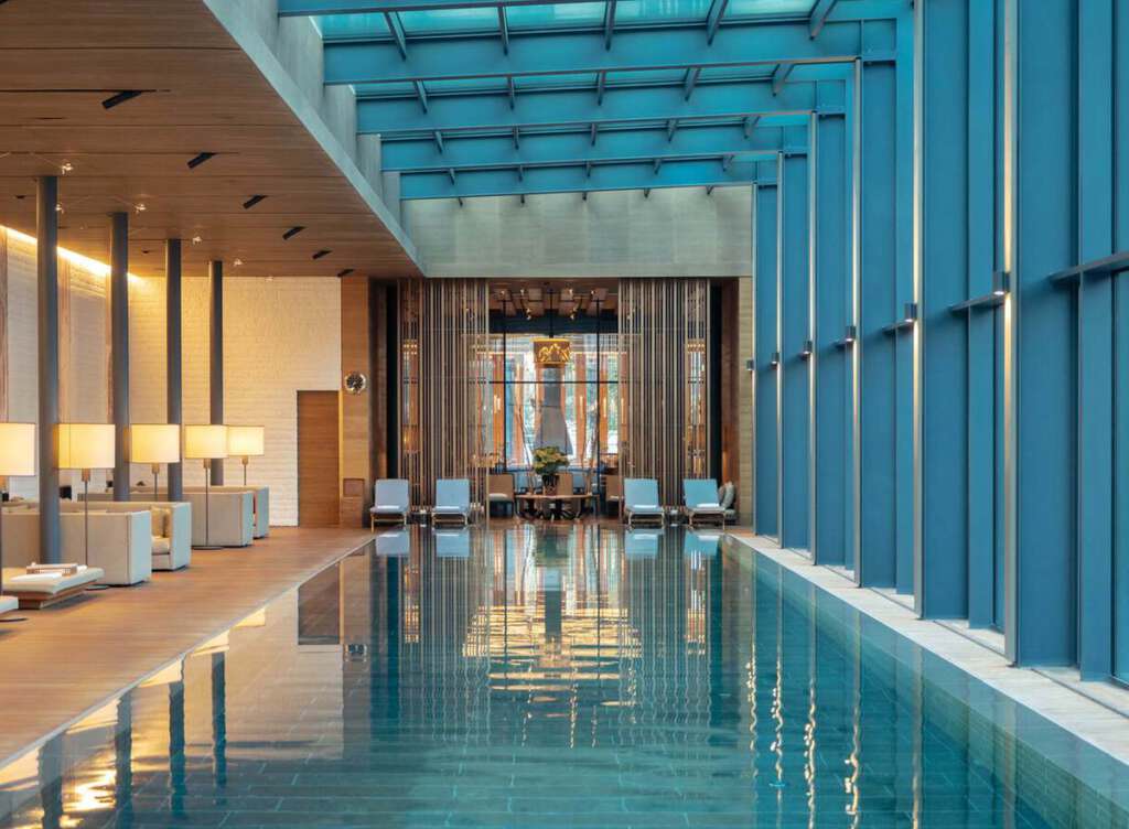 Innenpool mit modernem Design mit Holzakzenten und großen Fenstern. Liegestühle und sanfte Beleuchtung sorgen für eine entspannende Atmosphäre.