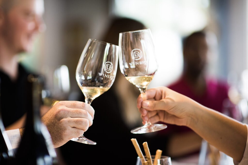 Menschen stoßen in geselliger Runde mit Weingläsern an, mit unscharfem Hintergrund und einer Flasche in der Nähe.