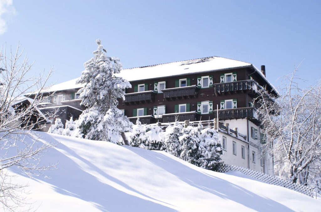 Ein großes Gebäude im Chalet-Stil mit schneebedeckten Bäumen und einem schneebedeckten Hang unter einem klaren blauen Himmel.