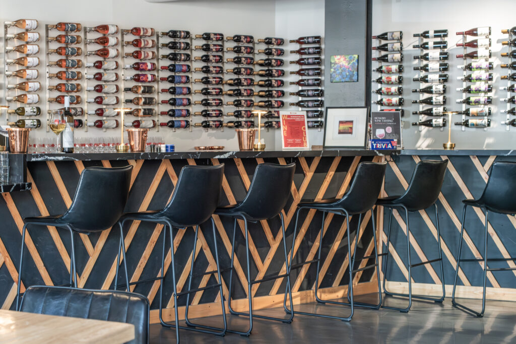 Eine moderne Bar mit schwarzen Hockern, einer geometrischen Holztheke und Wänden voller Weinflaschen.