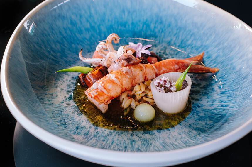 Gourmetgericht mit Garnelen und Tintenfisch, garniert mit kleinem Gemüse, serviert in einer blauen Keramikschüssel.