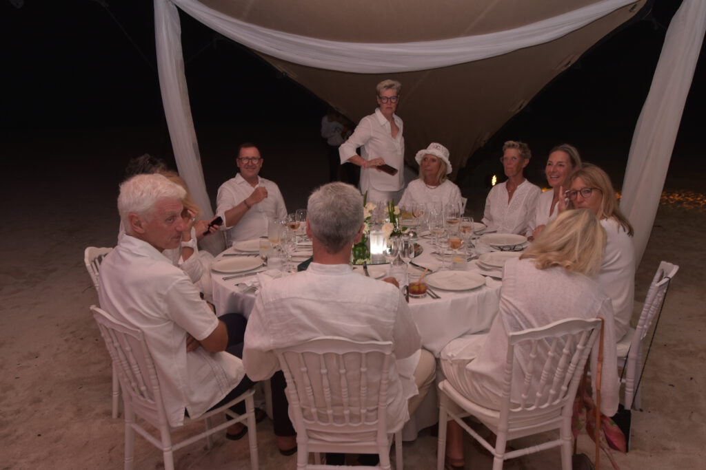 Eine Gruppe von Menschen in weißer Kleidung sitzt nachts im Freien um einen Tisch mit einem Baldachin darüber.