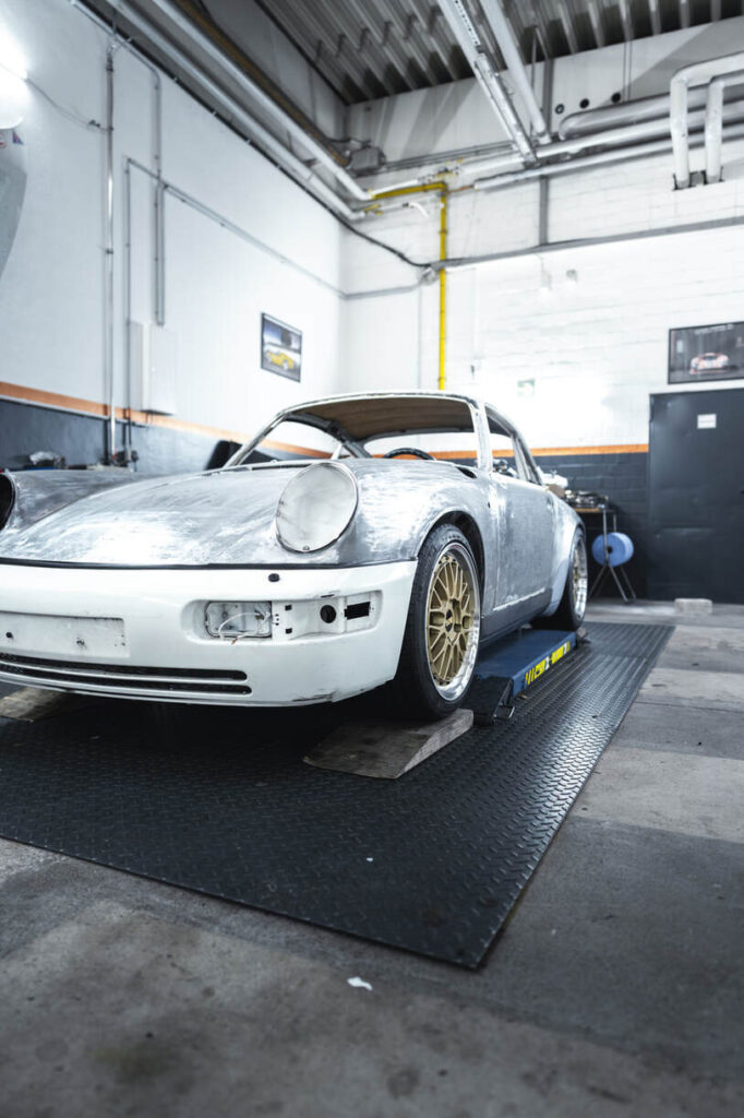 Ein teilweise restaurierter Oldtimer mit unfertiger Metallkarosserie auf einer Hebebühne in einer Garage.
