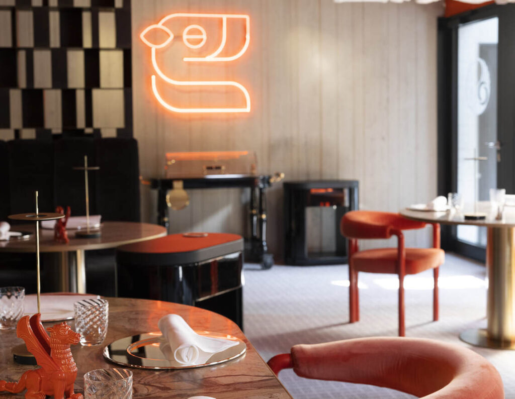 Zeitgenössisches Restaurant-Interieur mit modernem Dekor, mit roter Neonlichtkunst an der Wand, runden Tischen mit Gläsern und Servietten und roten Stühlen.