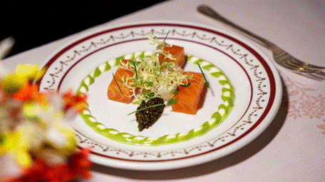 Ein Tellergericht mit drei Lachsstücken, einem Klecks Kaviar, grüner Soße und Mikrogrün auf einem dekorativen weißen Teller.