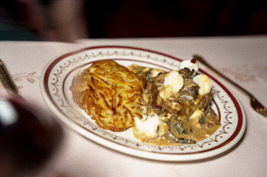 Ein Teller mit einer Portion knuspriger Rösti und einem cremigen Pilz- und Fleischgericht, garniert mit geschnittenen Pilzen und einer Kirsche.